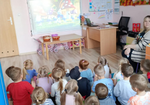 Dzieci oglądają bajkę wyświetlaną na ekranie w sali.