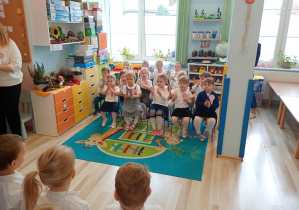 Dzieci młodsze po wspólnym odśpiewaniu hymnu, siedzą na krzesłach i aktywnie słuchają piosenek o charakterze patriotycznym śpiewanych przez kolegów z przedszkola.