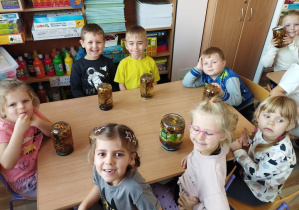 Uśmiechnięte dzieci siedzą przy stole i prezentują swój jesienny słoik