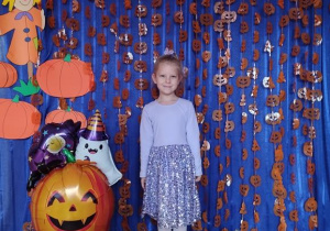Dziecko pozuje na tle dyniowej dekoracji