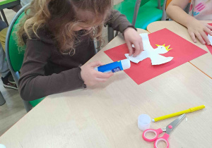 Dziewczynka wykonuje pracę - przykleja wycięty kształt orła