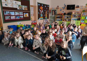 Dzieci siedzą na dywanie i oglądają prezentację na temat praw dziecka