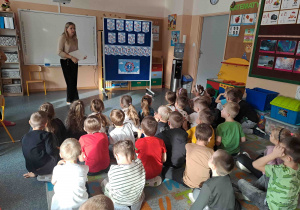 Dzieci siedzą na dywanie i oglądają prezentację na temat praw dziecka