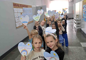 Dzieci na korytarzu szkolnym pokazują wykonane serduszka