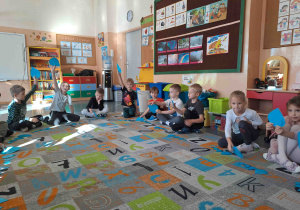 Dzieci siedzą w kole na dywanie i wykonują ćwiczenia z wykorzystaniem kropel deszczu w różnych rozmiarach