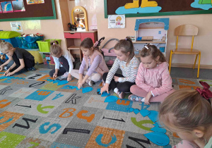 Dzieci siedzą w kole na dywanie i wykonują ćwiczenia z wykorzystaniem kropel deszczu w różnych rozmiarach