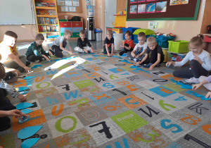 Dzieci siedzą w kole na dywanie i wykonują ćwiczenia z wykorzystaniem kropel deszczu w różnych rozmiarach