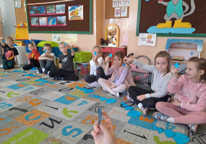 Dzieci siedzą w kole na dywanie i wykonują ćwiczenia z wykorzystaniem kropel deszczu w różnych rozmiarach