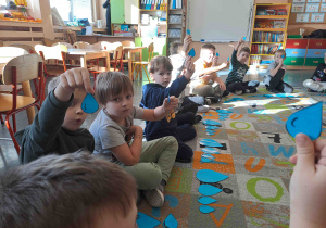 Dzieci siedzą w kole na dywanie i wykonują ćwiczenia z wykorzystaniem kropel deszczu w różnych rozmiarach