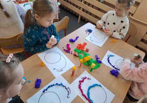 Dzieci wylepiają duży kształt cyfry bibułkowymi kuleczkami