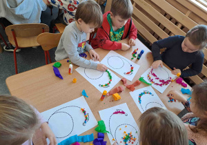 Dzieci wylepiają duży kształt cyfry bibułkowymi kuleczkami