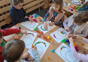 Dzieci wylepiają duży kształt cyfry bibułkowymi kuleczkami