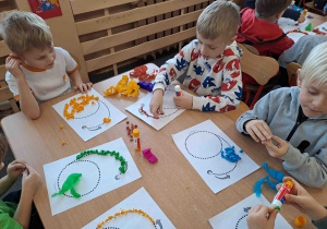 Dzieci wylepiają duży kształt cyfry bibułkowymi kuleczkami