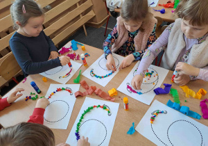 Dzieci wylepiają duży kształt cyfry bibułkowymi kuleczkami