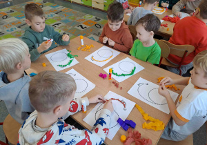 Dzieci wylepiają duży kształt cyfry bibułkowymi kuleczkami