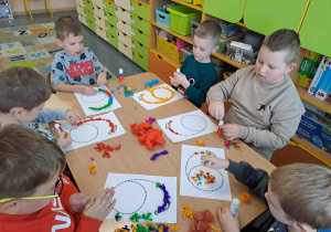 Dzieci wylepiają duży kształt cyfry bibułkowymi kuleczkami