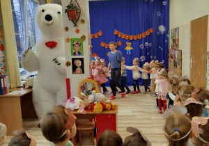 Dzieci wspólnie z białym misiem tworzą "pociąg"