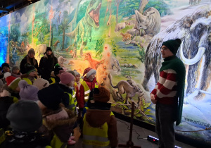 Dzieci w Muzeum Ziemi słuchają przewodnika, który opowiada ciekawostki.