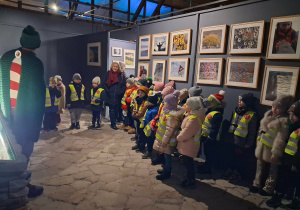 Dzieci w Muzeum Ziemi słuchają przewodnika, który opowiada ciekawostki