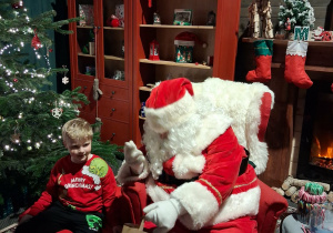 Dzieci siadają obok Świętego Mikołaja chwilkę rozmawiają a na zakończenie Mikołaj wręcza prezent dziecku.