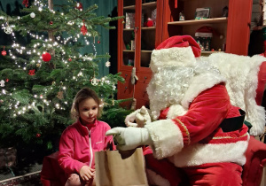 Dzieci siadają obok Świętego Mikołaja chwilkę rozmawiają a na zakończenie Mikołaj wręcza prezent dziecku.