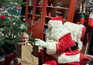 Dzieci siadają obok Świętego Mikołaja chwilkę rozmawiają a na zakończenie Mikołaj wręcza prezent dziecku.