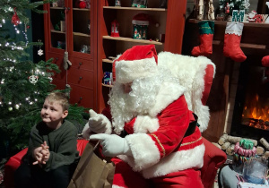 Dzieci siadają obok Świętego Mikołaja chwilkę rozmawiają a na zakończenie Mikołaj wręcza prezent dziecku.