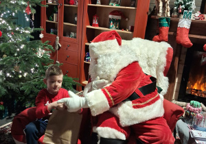 Dzieci siadają obok Świętego Mikołaja chwilkę rozmawiają a na zakończenie Mikołaj wręcza prezent dziecku.