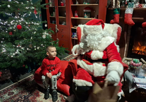 Dzieci siadają obok Świętego Mikołaja chwilkę rozmawiają a na zakończenie Mikołaj wręcza prezent dziecku.