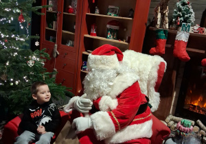 Dzieci siadają obok Świętego Mikołaja chwilkę rozmawiają a na zakończenie Mikołaj wręcza prezent dziecku.