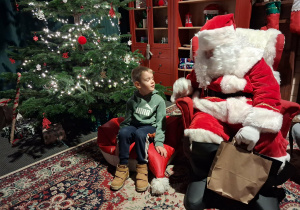 Dzieci siadają obok Świętego Mikołaja chwilkę rozmawiają a na zakończenie Mikołaj wręcza prezent dziecku.