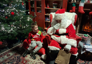 Dzieci siadają obok Świętego Mikołaja chwilkę rozmawiają a na zakończenie Mikołaj wręcza prezent dziecku.