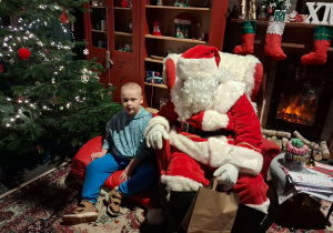 Dzieci siadają obok Świętego Mikołaja chwilkę rozmawiają a na zakończenie Mikołaj wręcza prezent dziecku.