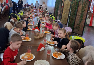 Dzieci siedzą przy stole i jedzą obiad.