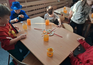 Dzieci wykonują lampiony przy stoliku. Malują farbami słoiki i naklejają ozdoby.