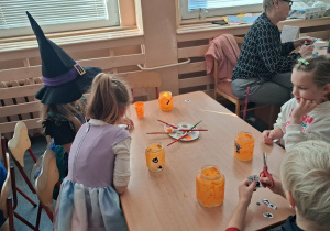 Dzieci wykonują lampiony przy stoliku. Malują farbami słoiki i naklejają ozdoby.