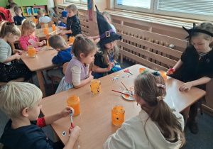 Dzieci wykonują lampiony przy stoliku. Malują farbami słoiki i naklejają ozdoby.