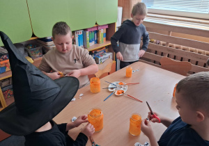 Dzieci wykonują lampiony przy stoliku. Malują farbami słoiki i naklejają ozdoby.