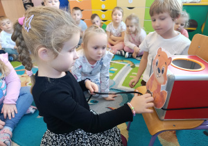 Dziewczynka nawleka żołędzia na sznurek i wykonuje ćwiczenie artykulacyjne