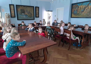 Dzieci w siedzą przy stołach i oglądają prezentację multimedialną poświęconą strojom dworskim
