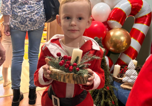 Chłopiec w stroju św. Mikołaja trzyma stroik bożonarodzeniowy