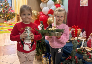 Jedna z dziewczynek trzyma słoik z pieniążkami, druga-stroik