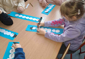 Dzieci wycinają i układają papierowe kółka w kształt bałwanka
