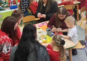 Dzieci przy stolikach z Rodzicami ozdabiają kartki świąteczne