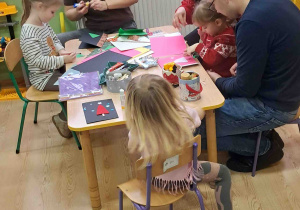 Dzieci przy stolikach z Rodzicami ozdabiają kartki świąteczne