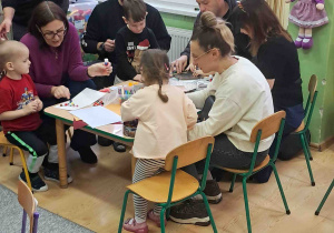 Dzieci przy stolikach z Rodzicami ozdabiają kartki świąteczne