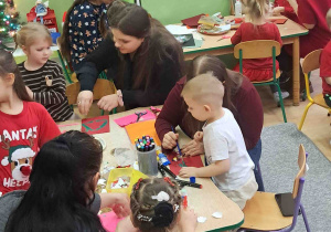 Dzieci przy stolikach z Rodzicami ozdabiają kartki świąteczne