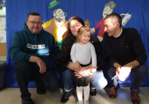 Babcie i dziadkowie kucają na tle dekoracji z wnuczką