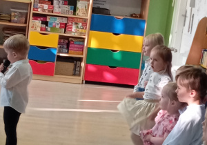 Chłopiec w czarnych spodniach i białej koszuli mówi wiersz