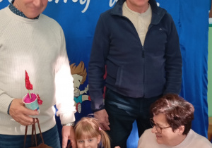 Dziewczynka stoi na tle dekoracji z babciami i dziadkami